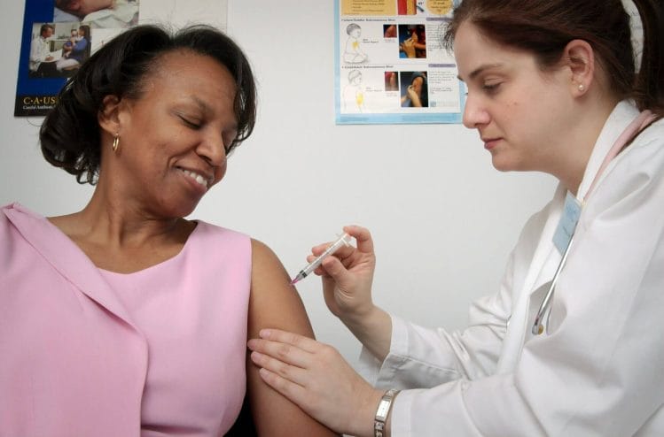Mujer aplicando vacuna a otra. DHS no tendrá en cuenta el estatus migratorio para el acceso a la vacuna