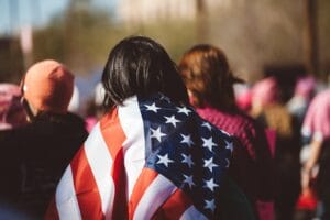 mujer con bandera de estados unidos en su espalda - este artículo habla acerca de los peligros que corre el programa DACA y los dreamers